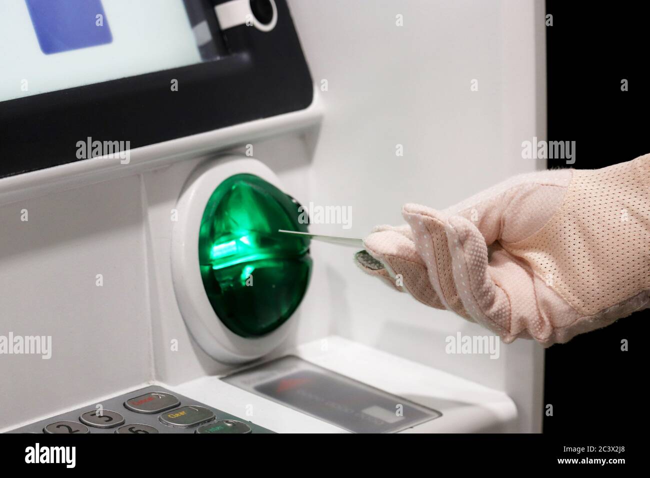 Frau legt eine Bankkarte in den ATM-Empfänger ein. Weibliche Hand im Schutzhandschuh, finanzielle Transaktionen und Sicherheitsmaßnahmen während der covid-19 Stockfoto