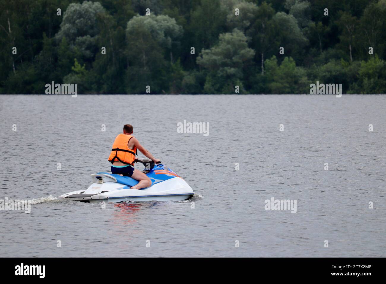 Man in Life Weste reitet einen Wasserscooter auf dem Fluss auf Waldgrund. Sicherheit auf dem Wasser während der Sommerferien Stockfoto