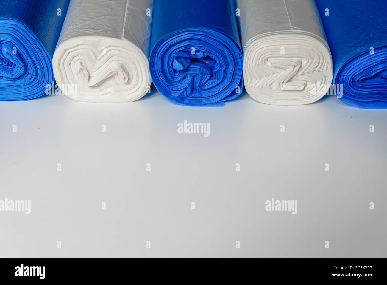 Blaue und weiße Plastikmüllbeutel in einer obersten Reihe auf einer weißen Oberfläche. Recycelbare Materialien zum Schutz der Umwelt während der Isolierung von Coronaviren. Stockfoto
