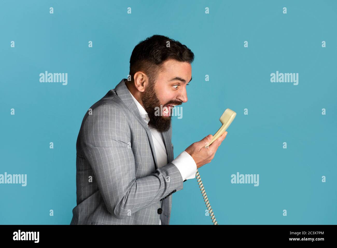 Arbeitsstress. Wütend Geschäftsmann schreien in Festnetz-Telefon-Empfänger vor blauem Hintergrund Stockfoto