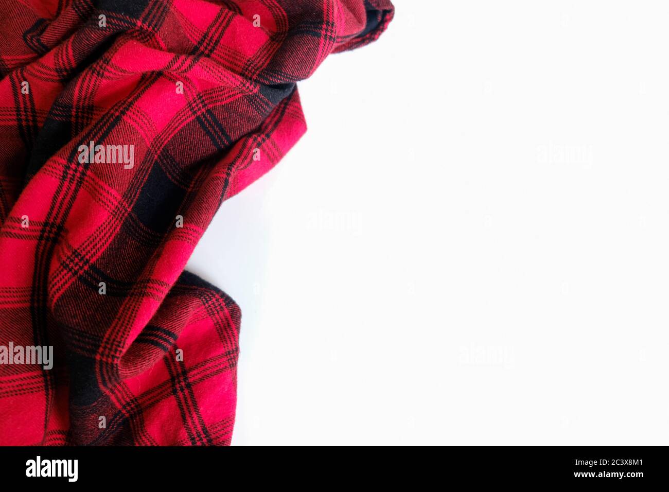 Knittertes Hemd in leuchtendem Rot auf weißem Hintergrund. Umgebung für Arbeit oder Studium von zu Hause aus. Leere Oberfläche, umgeben von weichem, warmem Material. Stockfoto
