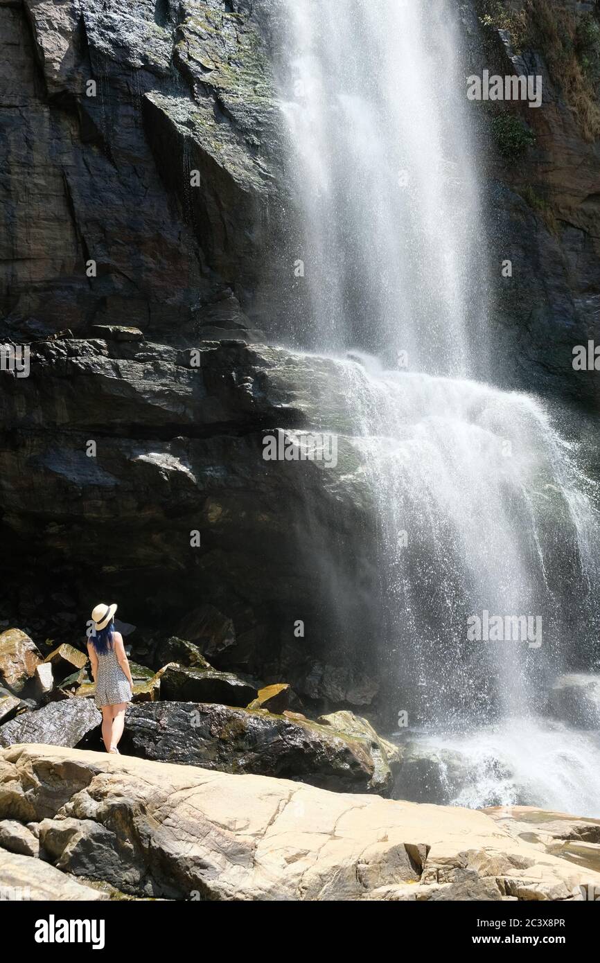 Blauhaariges Mädchen in einem Hut unter Ramboda Wasserfall in Sri Lanka. Beobachten Sie das Wasser fließt an einem beliebten touristischen Aussichtspunkt in Ella. Stockfoto
