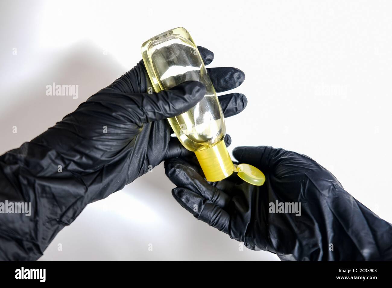 Zwei Hände in schwarzen Handschuhen, die Handdesinfektionsmittel aus einer kleinen gelben Flasche auf weißem Hintergrund auftragen. Desinfizieren von Oberflächen, um in Isolation gesund zu bleiben Stockfoto