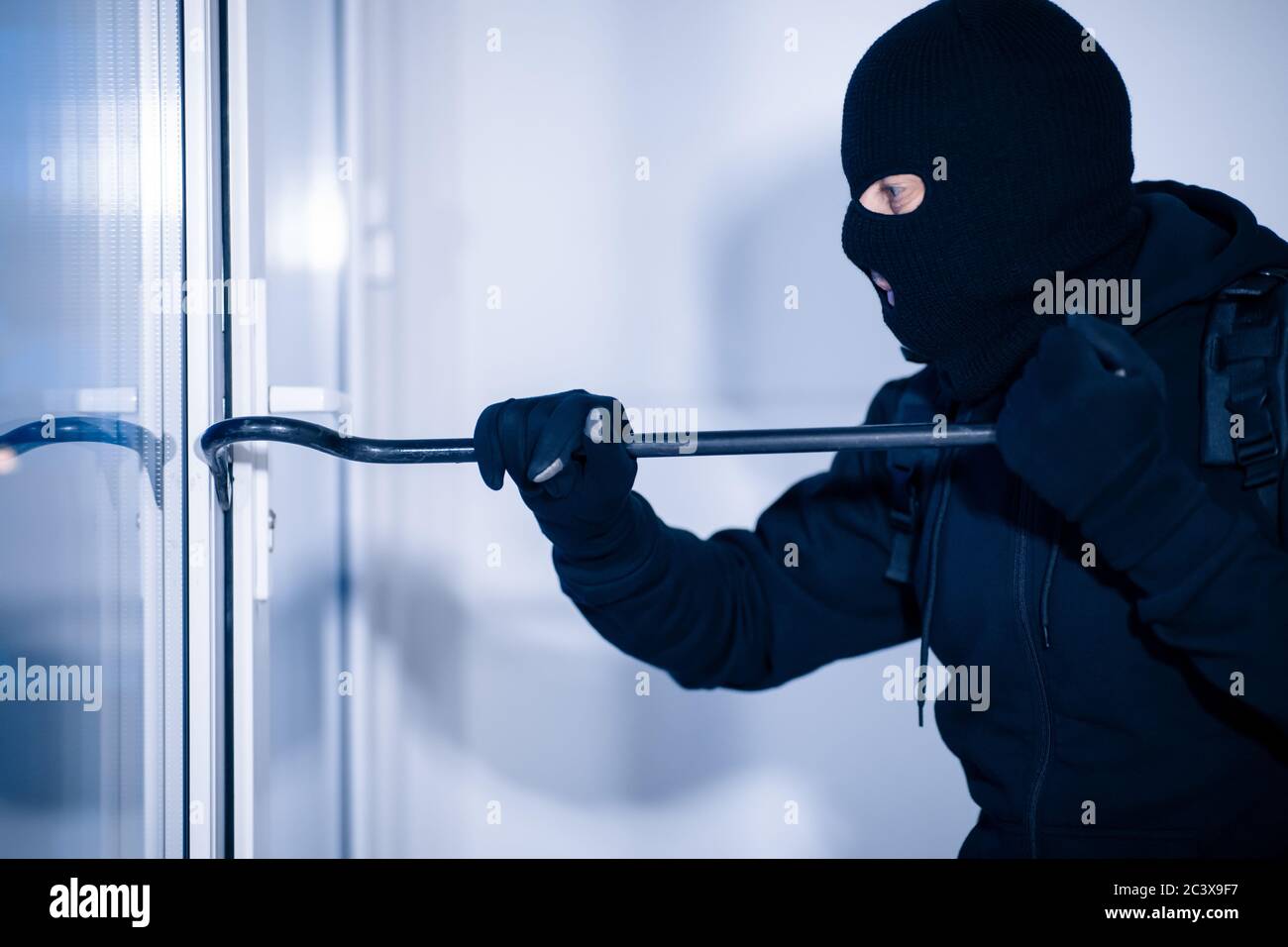 Räuber in schwarzer Balaclava Risse Tür mit dem Brecheisen Stockfoto