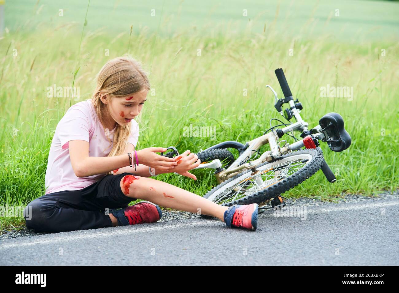 Trauriger weinender kleiner Kindermädchen fiel vom Fahrrad im Sommerpark. Blutungen an Händen und Füßen. Fahrradunfall. Verletzungen beim Radfahren. Stockfoto