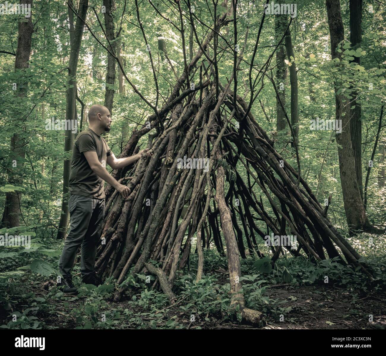 Mann, der im Wald ein Überlebensheim baut. Schutz im Wald vor Ästen. Stockfoto