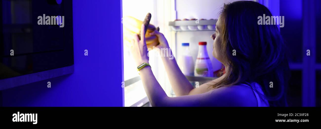 Frau in der Nacht geöffnet Kühlschrank und nimmt Essen Stockfoto