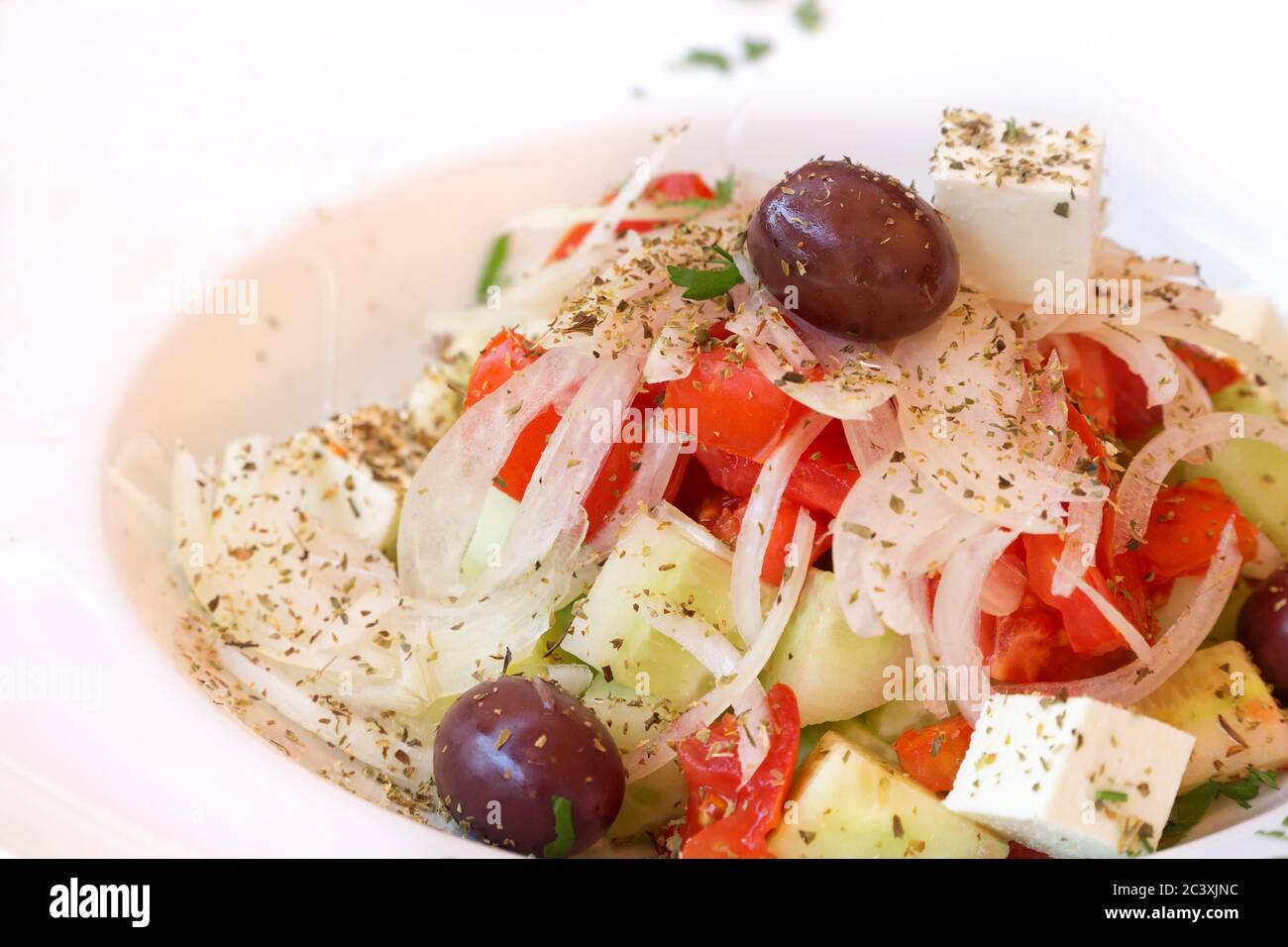 Frischer Frühlingssalat mit Tomaten, Gurken, Zwiebeln, schwarzen Oliven, Feta-Käse, Olivenöl, bestreut mit Kräutern, serviert auf weißem Teller mit Kopierplatz. Stockfoto