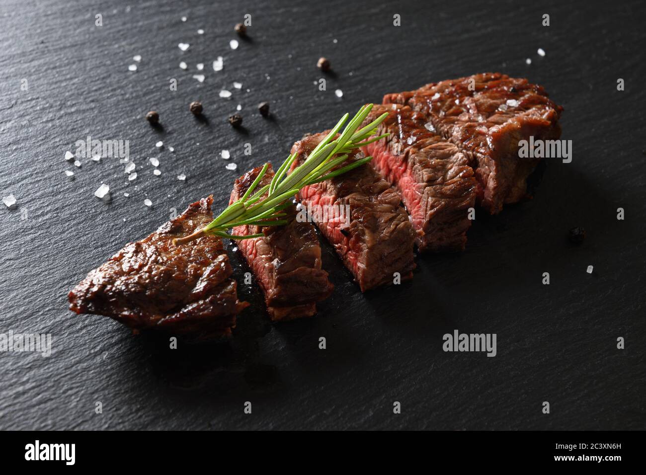 Frisch gegrilltes marmoriertes Rindersteak, mittelselten mit Rosmarin auf Schwarz. Stockfoto