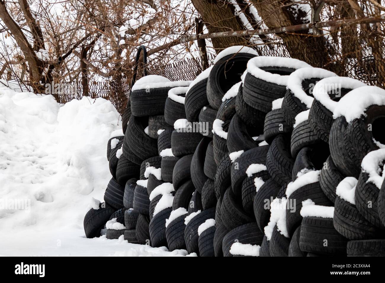 Autoreifen werden entlang eines Kettengliederzauns im Winter gestapelt, mit Schnee bedeckt Teile von ihnen. Stockfoto