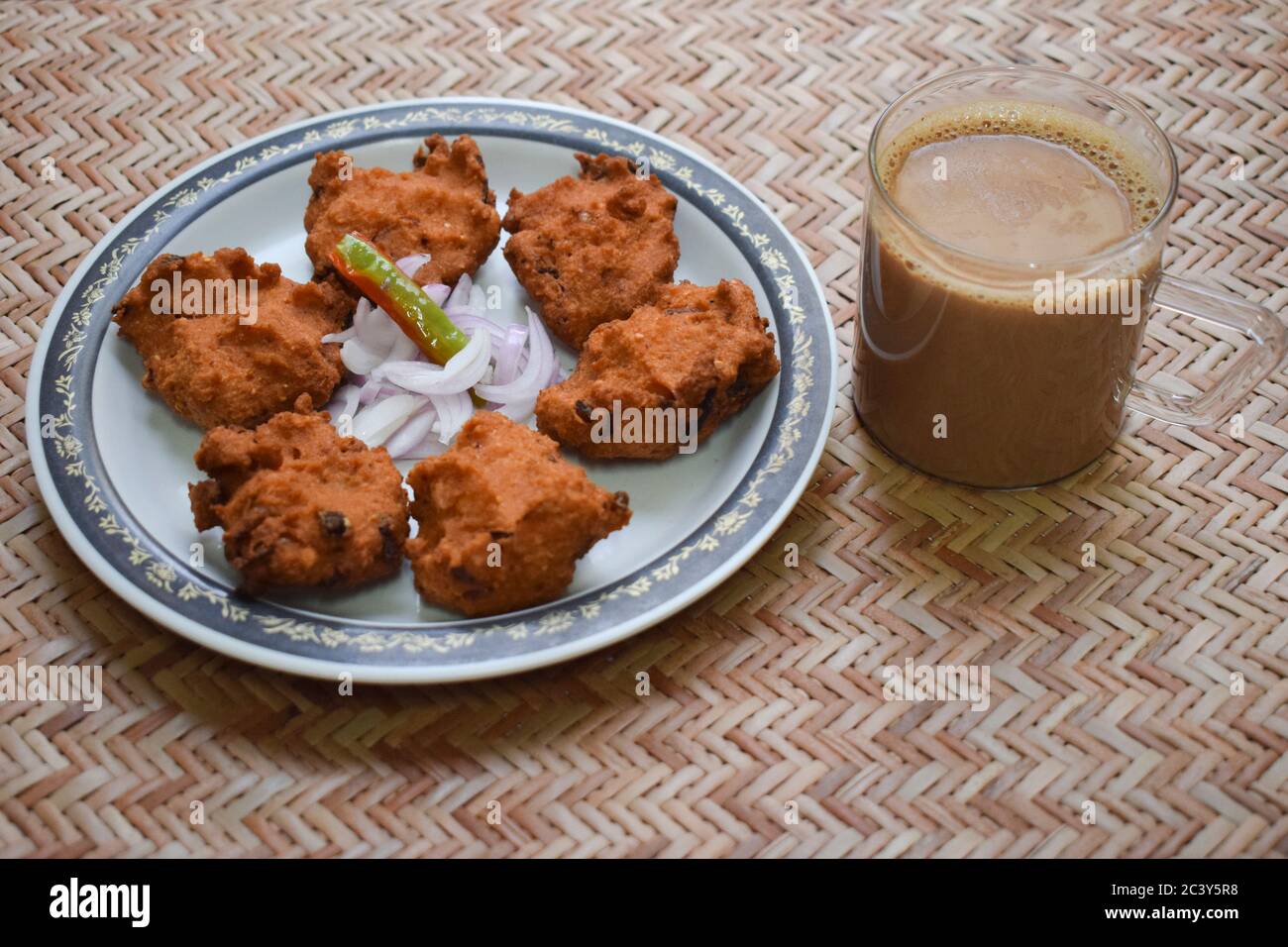 Seitenansicht von Dal vada, Masala vada, Chana vada serviert mit geschnittenen Zwiebeln und grünem Chilly und Tee auf der Serviermatte. Frittierte indische Küche Snacks, Linsen Stockfoto