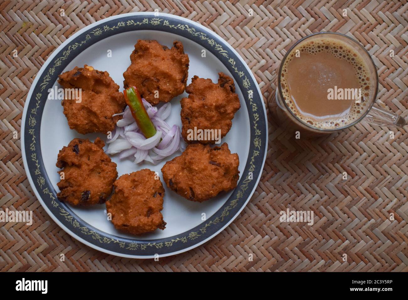 Draufsicht auf Dal vada, Masala vada, Chana vada serviert mit geschnittenen Zwiebeln und grünem Chilly und Tee auf Serviermatte. Frittierte indische Küche Snacks, Linsen Stockfoto