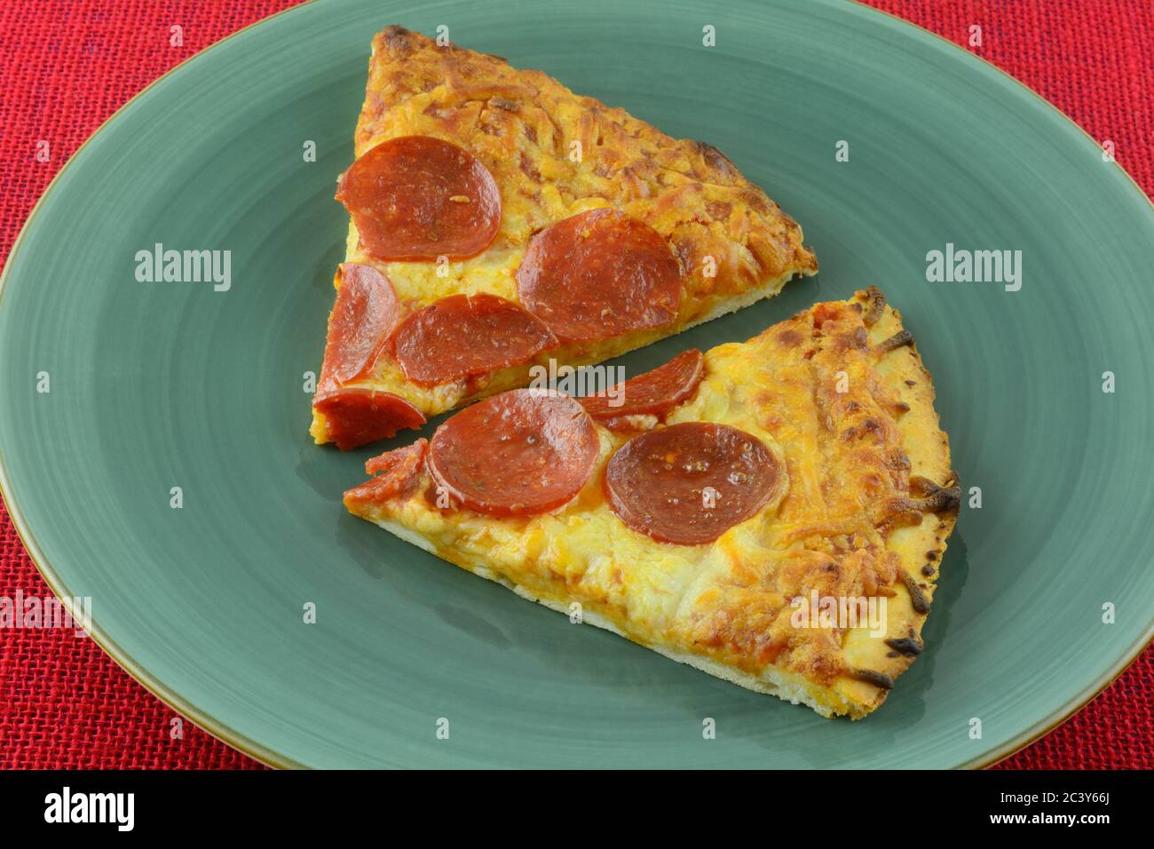 Zwei Scheiben gebackene Pepperoni Pizza auf blauem Teller auf roter Tischdecke Stockfoto