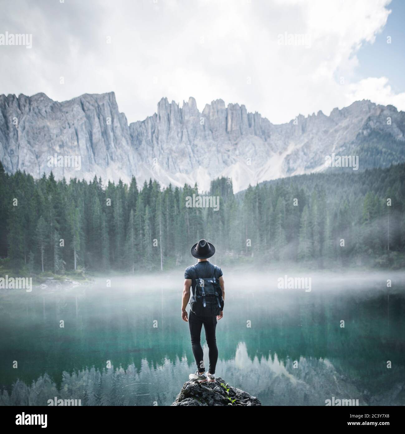 Italien, Karersee, junger Mann steht am Karersee in den Dolomiten bei Sonnenaufgang auf dem Felsen Stockfoto