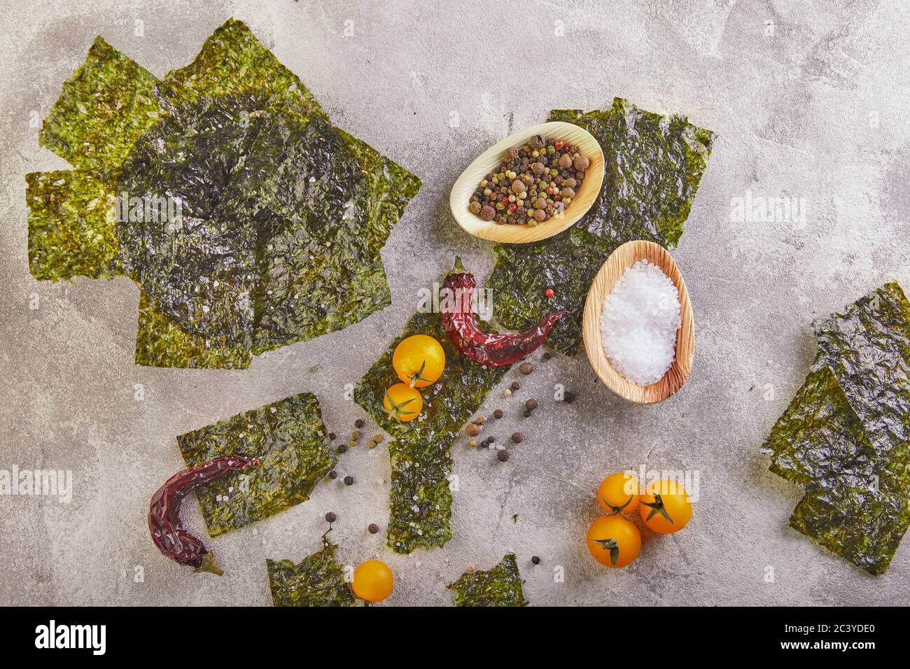 Knusprige Nori-Algen mit Kirschtomaten und Gewürzen auf grauem Beton. Japanisches Essen Nori. Getrocknete Blätter von Algen. Speicherplatz kopieren. Flach liegend Stockfoto