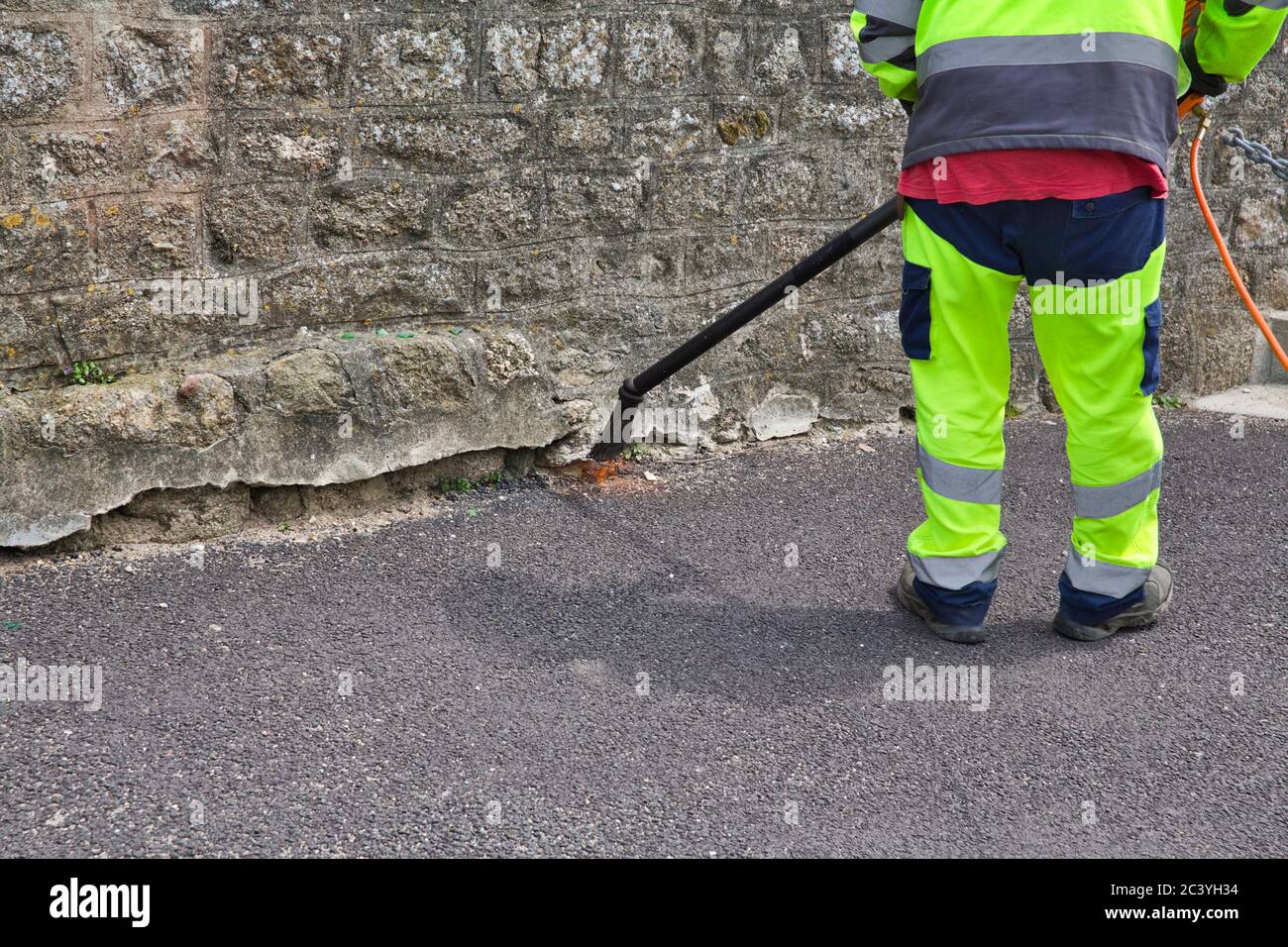 Mann, der Unkraut mit Gas in der Straße der Stadt verbrennt. Umweltschutz. Mit gelben Tüchern Stockfoto