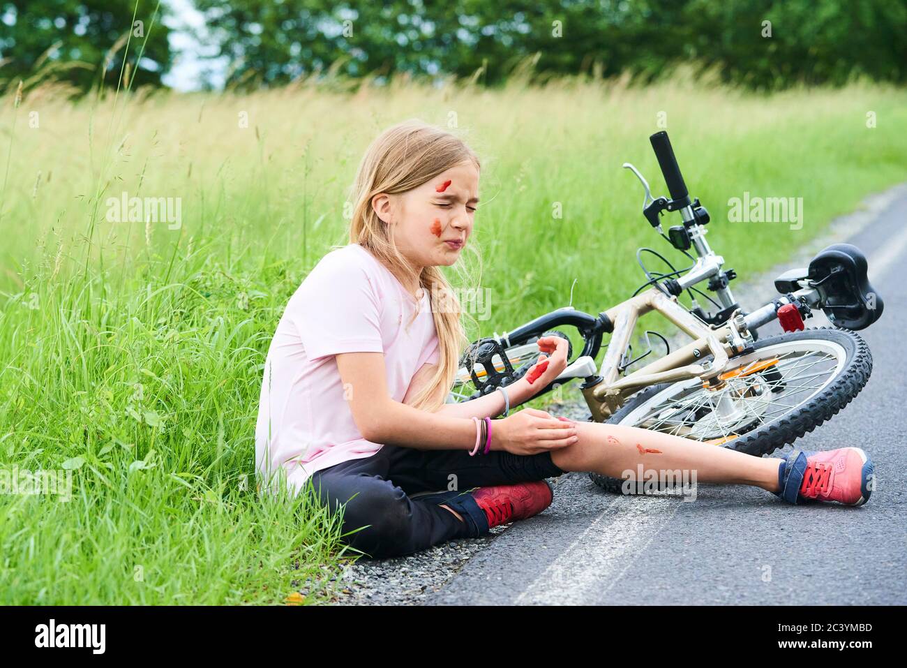 Trauriger weinender kleiner Kindermädchen fiel vom Fahrrad im Sommerpark. Blutungen an Händen und Füßen. Fahrradunfall. Verletzungen beim Radfahren. Stockfoto