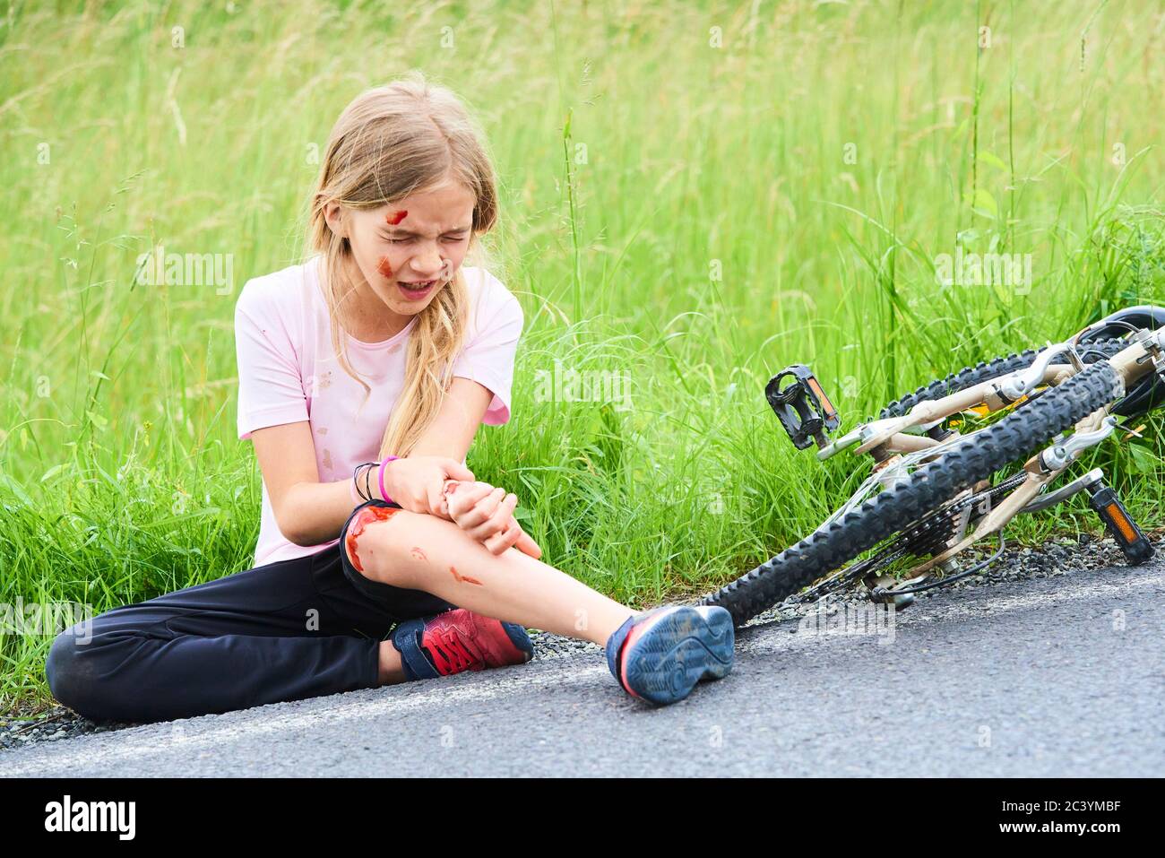 Trauriger weinender kleiner Kindermädchen fiel vom Fahrrad im Sommerpark. Blutungen an Händen und Füßen. Fahrradunfall. Verletzungen beim Radfahren. Stockfoto