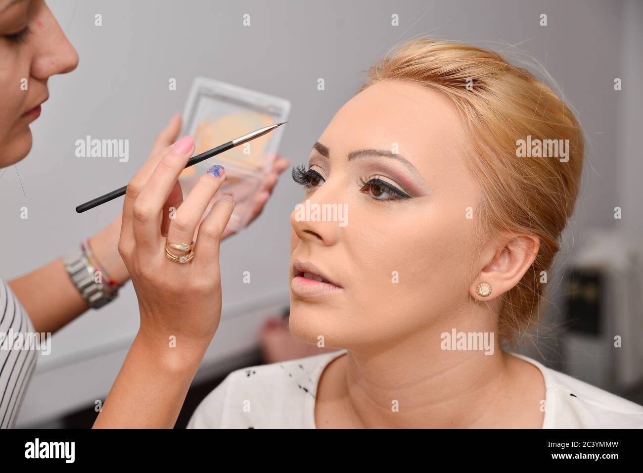 Prozess der Herstellung von Make-up. Make-up-Künstler arbeitet mit Pinsel auf Modell Gesicht. Porträt einer jungen Brünette Frau im Schönheitssalon Innenraum. Stockfoto