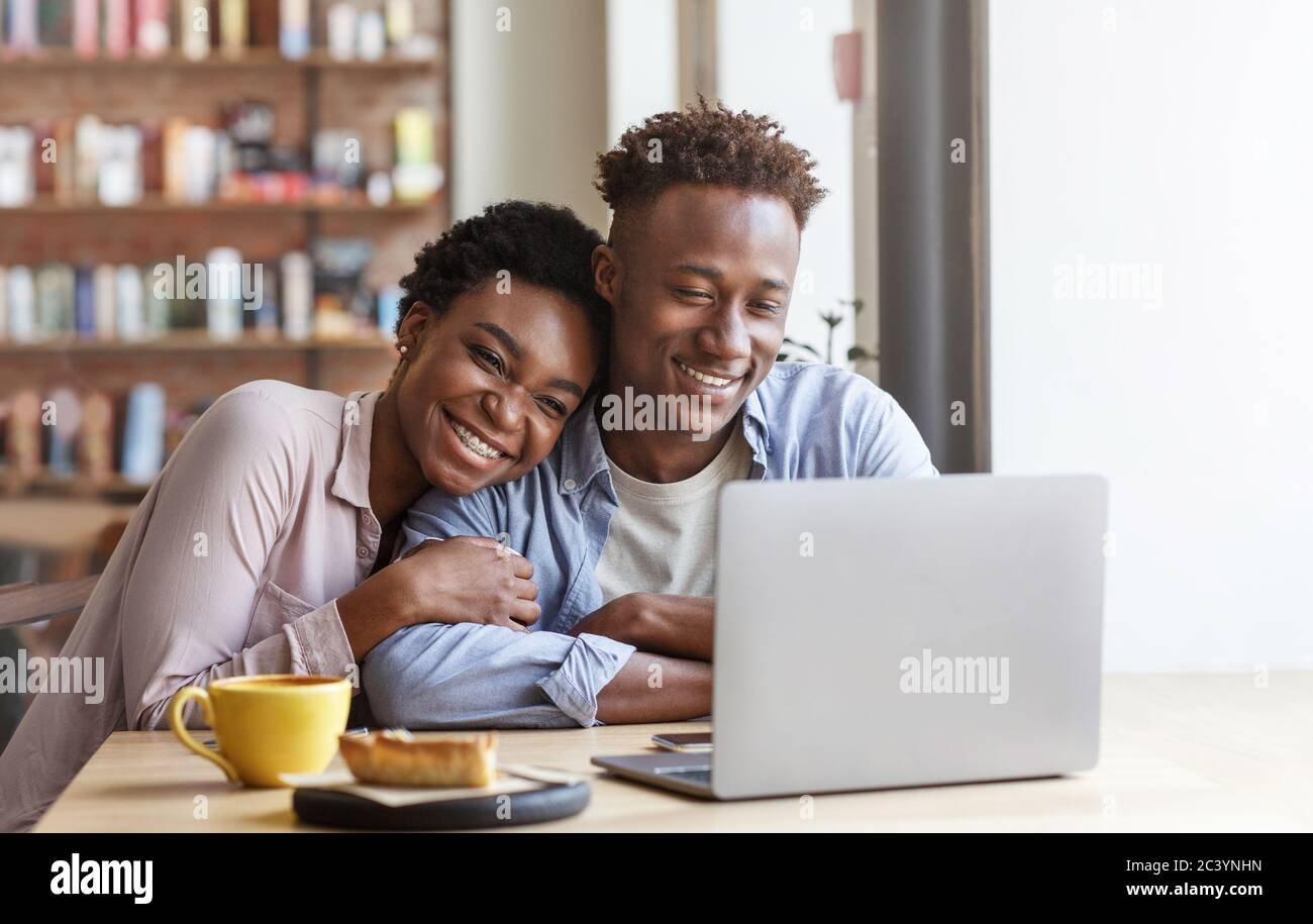 Afroamerikanisches Mädchen umarmt ihren Freund, während sie Film auf Laptop im Café ansieht Stockfoto