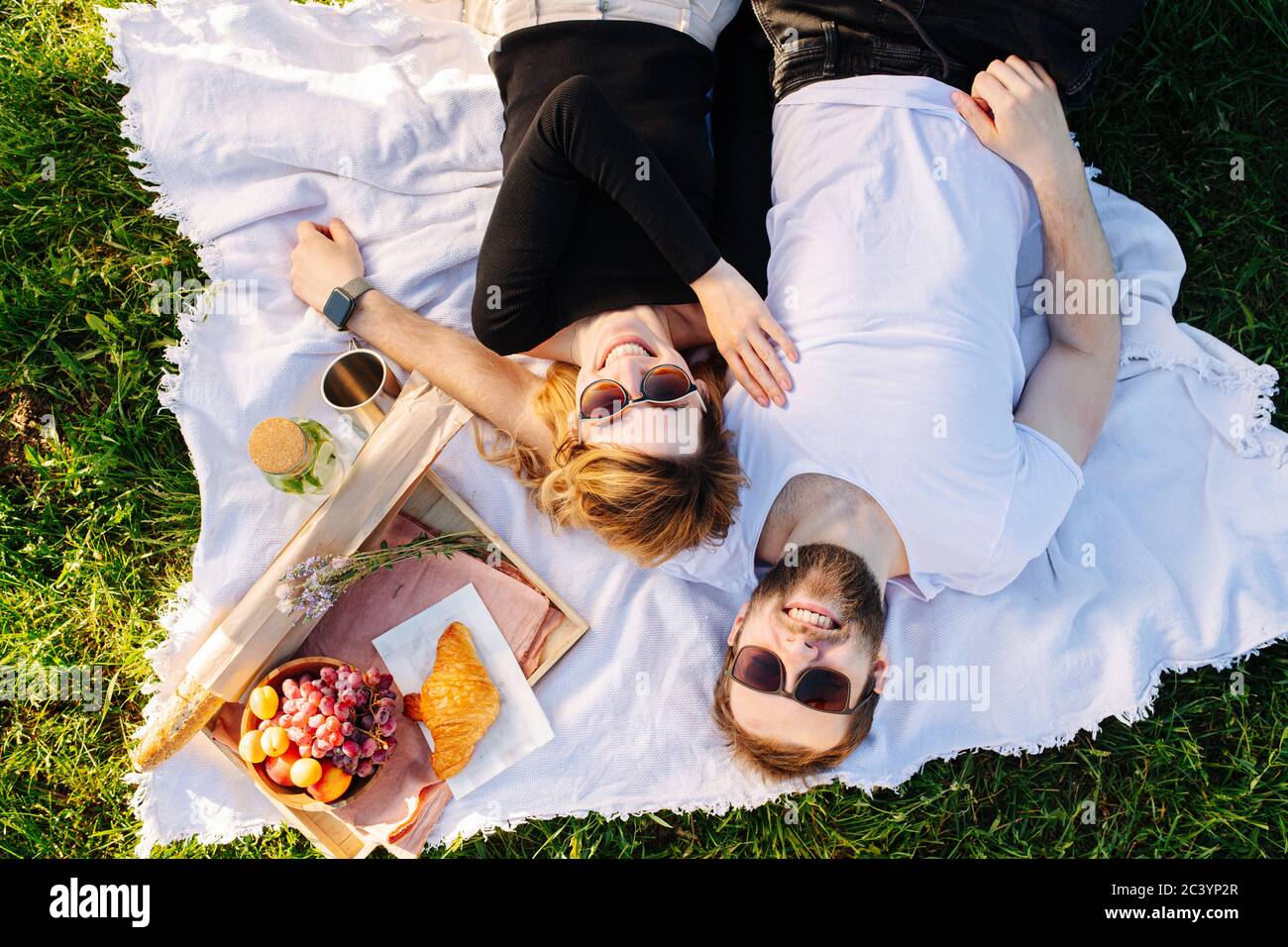 Glückliches Paar, das sich während des Picknicks auf einer Decke neben der Futterkiste ausruhte Stockfoto
