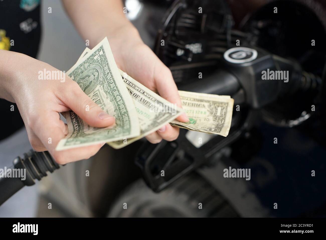Die Hände zählen zusammengeknitterte Dollarscheine vor dem Hintergrund der Betankung Auto Stockfoto