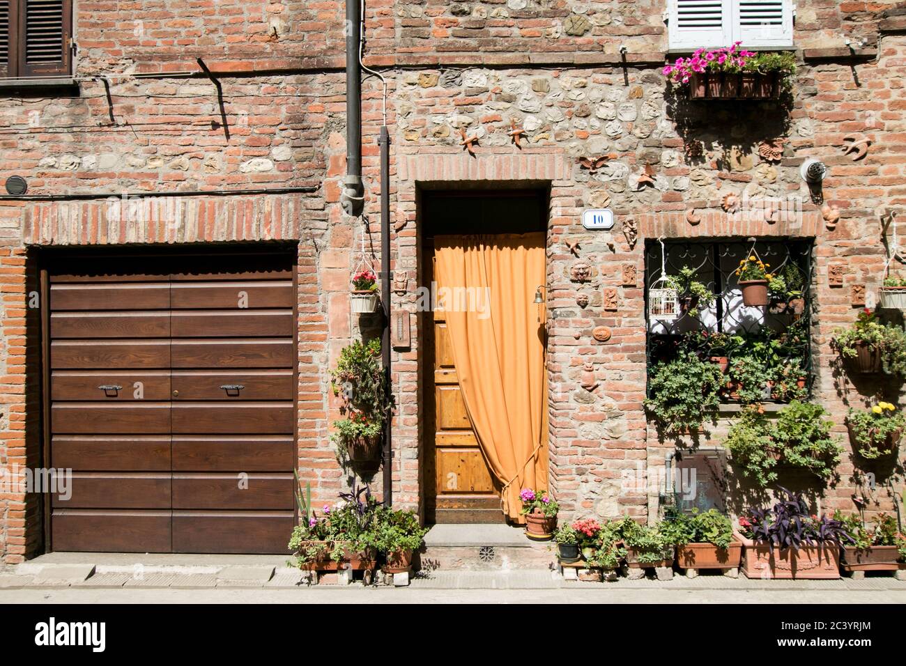 Typische Fassade eines Hauses in einem kleinen italienischen Dorf mit Ziegelmauer, hölzernen Eingang und blühenden Pflanzen in Töpfen Stockfoto