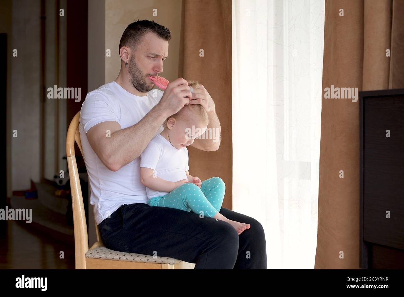 Ein junger Vater verbringt Zeit mit einer kleinen Tochter. Papa flechtschleif einen Pferdeschwanz Stockfoto