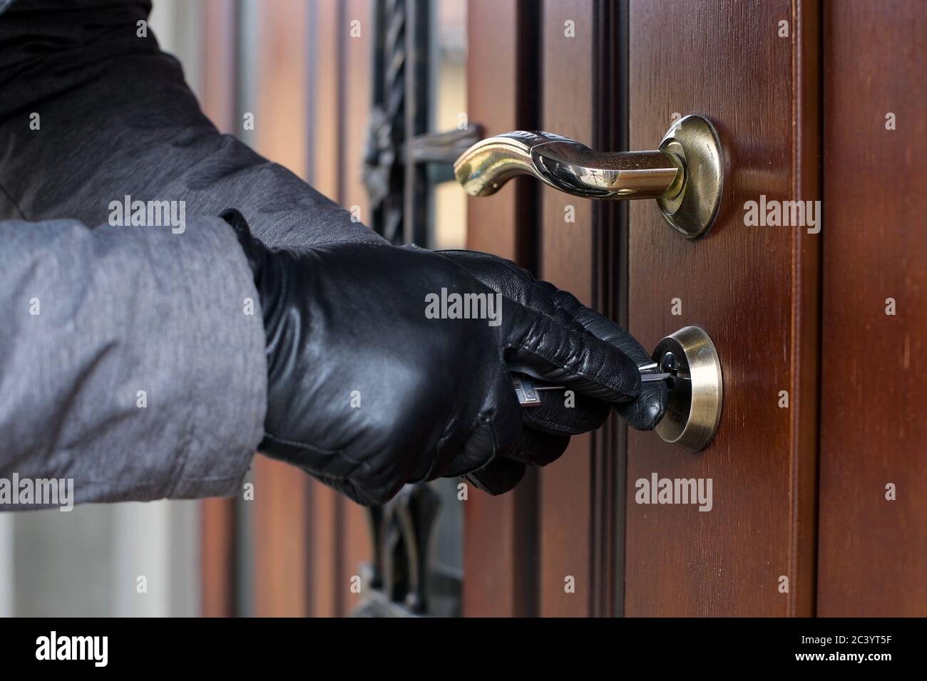 Ein Dieb in Handschuhen öffnet das Türschloss eines Privathaus und dringt nach innen Stockfoto