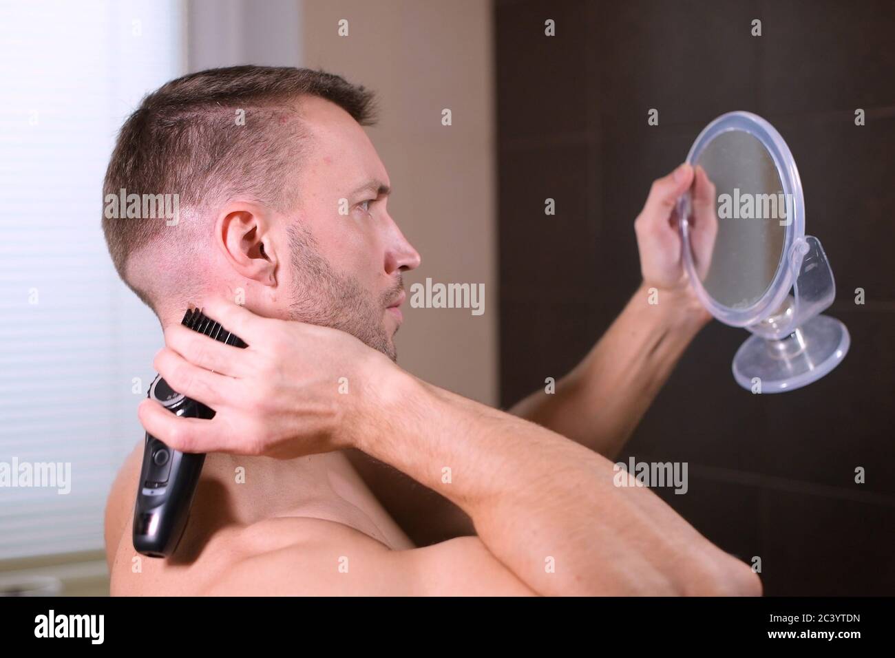 Ein junger Mann schneidet sich mit Spiegelspiegeln und einem Haarschneider Stockfoto