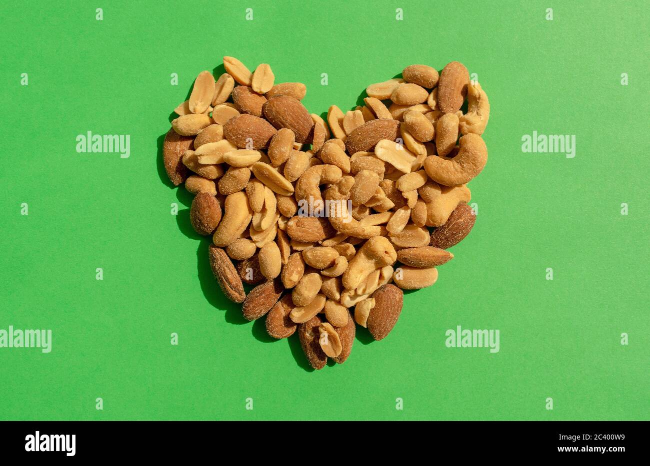 Verschiedene Nüsse bilden Herz-Form auf grünem Hintergrund. Draufsicht. Verschiedene Arten von leckeren und gesunden Nüssen, Snack. Stockfoto