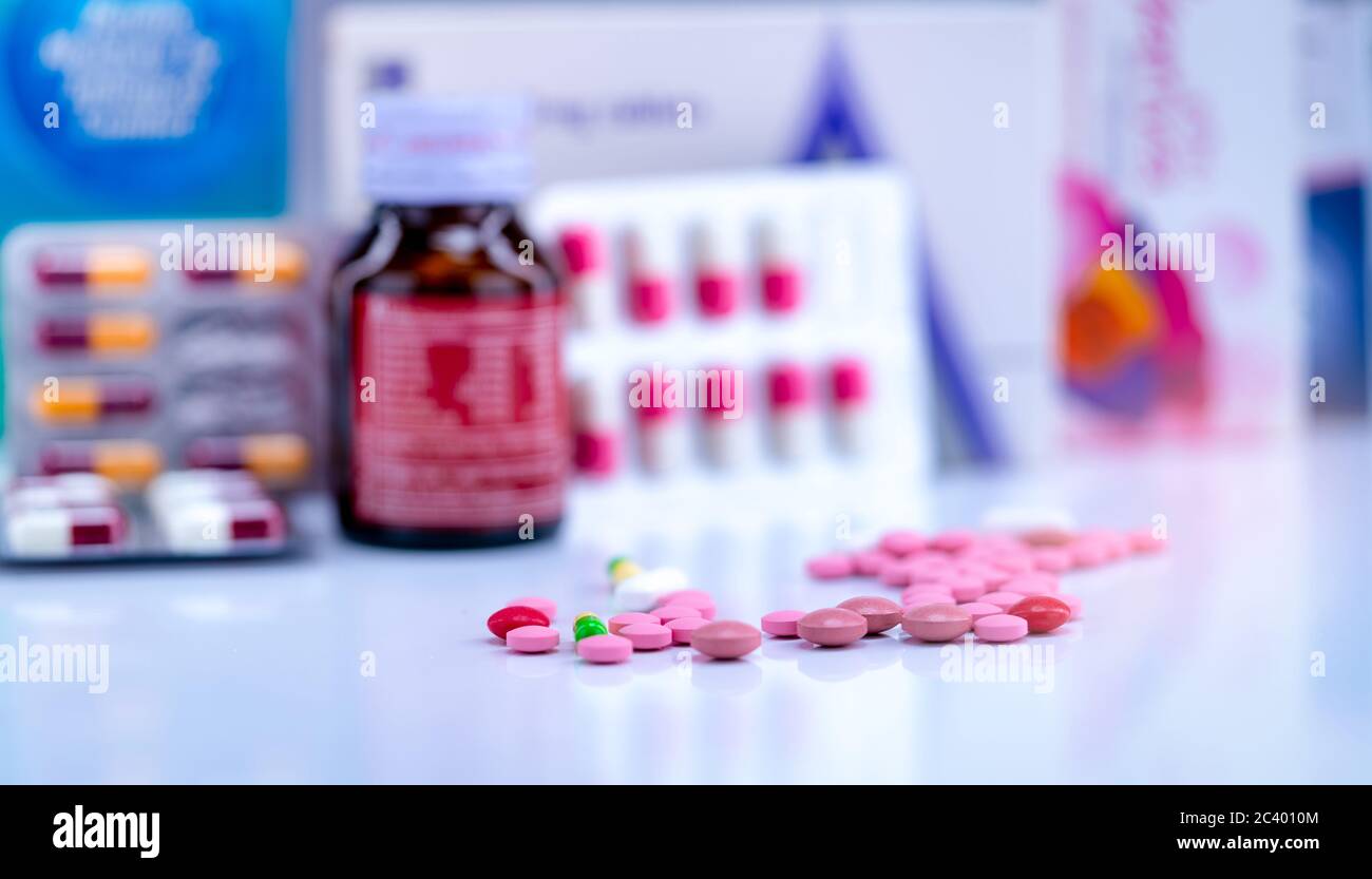 Tabletten und Kapseln Pillen auf verschwommene Drogenflasche, Kapsel in Blisterpackung und Papierkarton Packung Medizin. Rosa und rote Tabletten und grün-gelbe Kappe Stockfoto