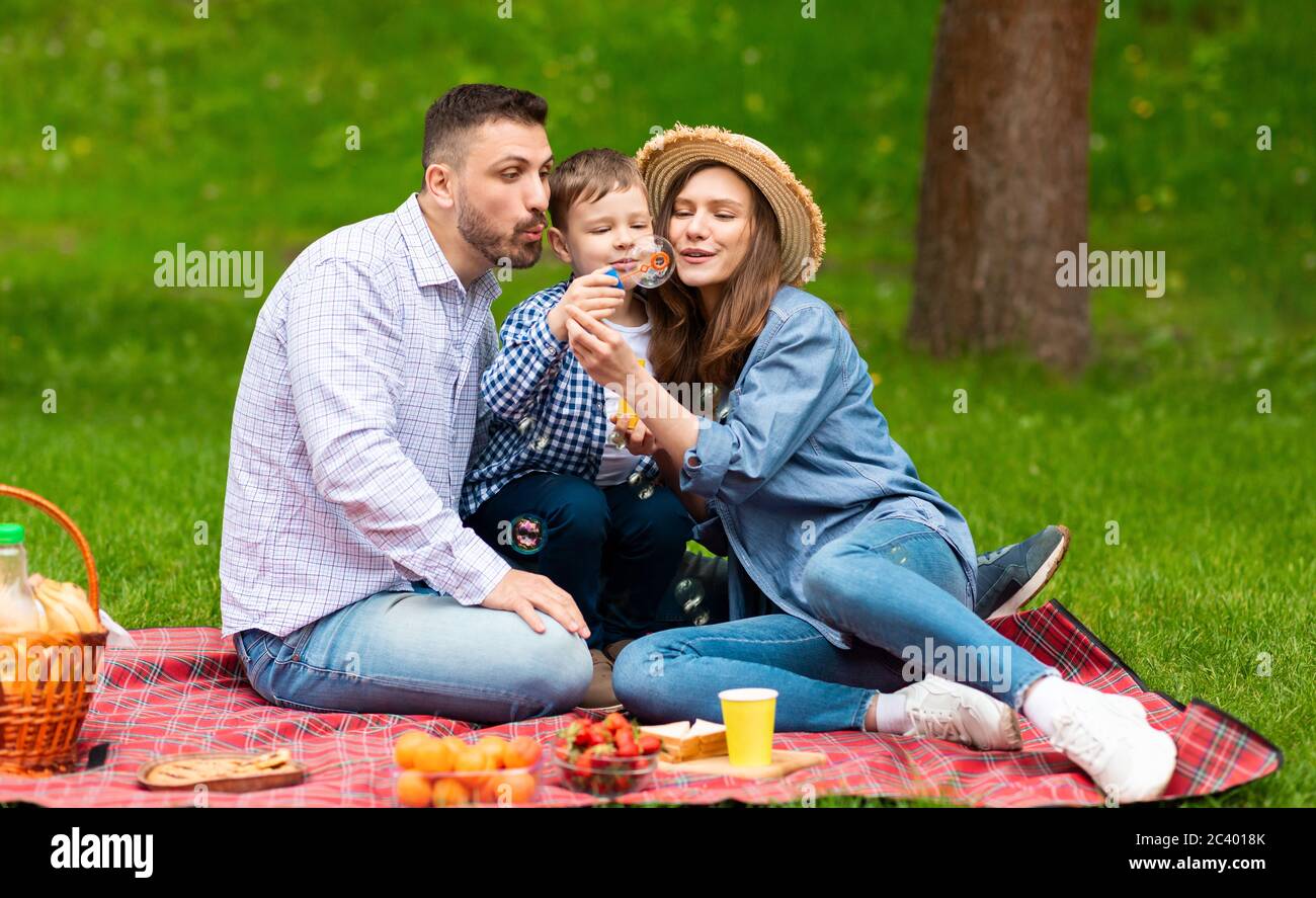 Sommer Picknick im Park. Millennial Eltern mit ihrem niedlichen Sohn Spaß mit Seifenblasen draußen Stockfoto