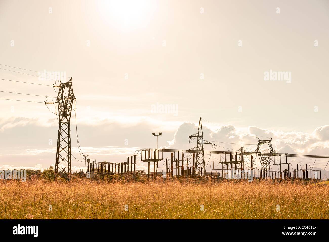 Elektrischer Pylon und Umrichterstation bei Sonnenuntergang, zwischen kultivierten Feldern. Stockfoto