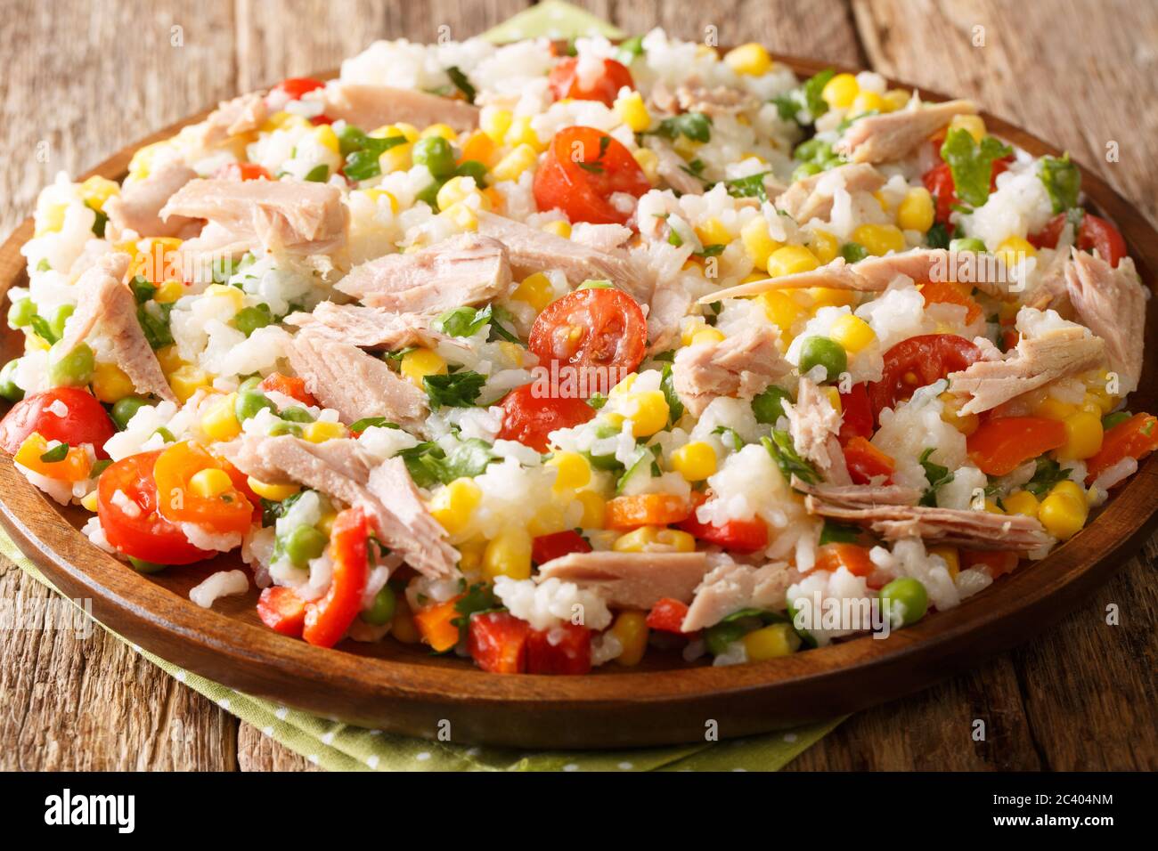 Gekochter Reis mit Thunfisch, Tomaten, Paprika, Mais, grünen Erbsen und Kräutern in Nahaufnahme auf einem Teller auf dem Tisch. Horizontal Stockfoto