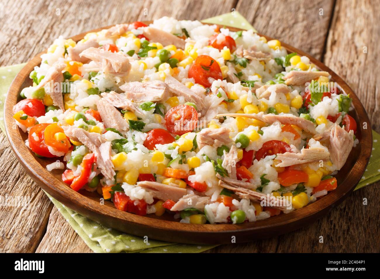 Salat aus Reis, Thunfisch, Tomaten, Paprika, Mais, grünen Erbsen und Kräutern in einer Platte auf dem Tisch. Horizontal Stockfoto