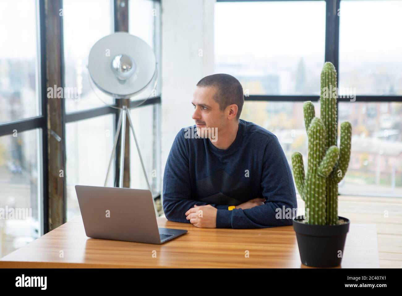 Mann, der mit einem Laptop am Schreibtisch saß und ins Fenster schaute Stockfoto