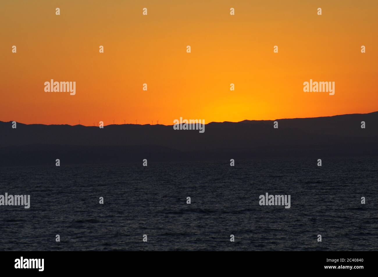 goldener Himmel über dunklem Meer, goldener Himmel über dunklem Ozean, gelbgoldener Himmel bei Sonnenuntergang über dem Meer, goldener Himmel und dunkles Meer, niedrige Berg Silhouette bei Stockfoto