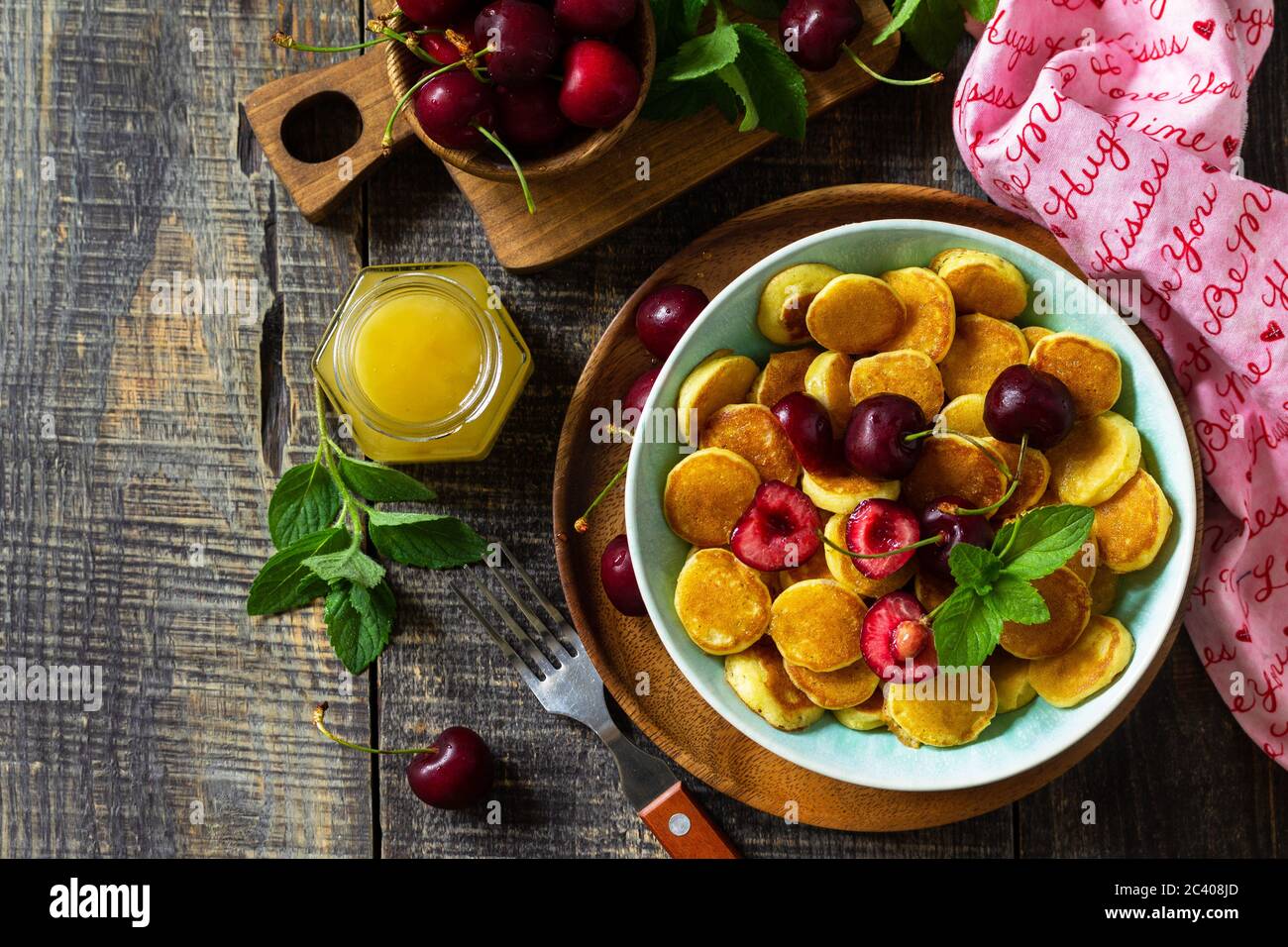 Winziges Pfannkuchen-Frühstück. Mini-Pfannkuchen mit Kirschen und Honig auf rustikalem Holztisch. Draufsicht flach lagen Hintergrund. Speicherplatz kopieren. Stockfoto