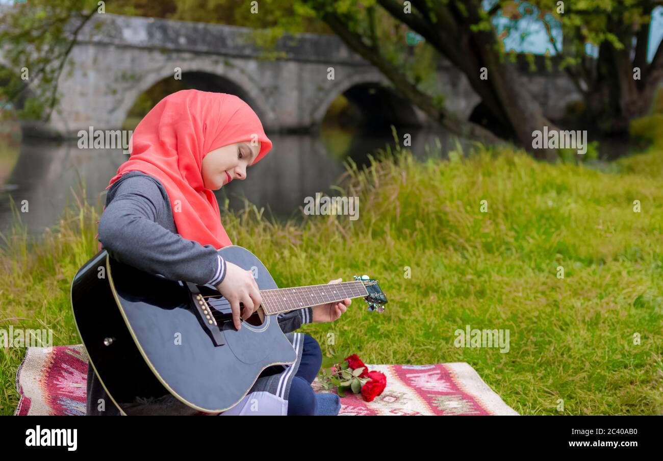 Ziemlich junge muslimische Mädchen versuchen, akustische Gitarre am Flussufer zu spielen Stockfoto
