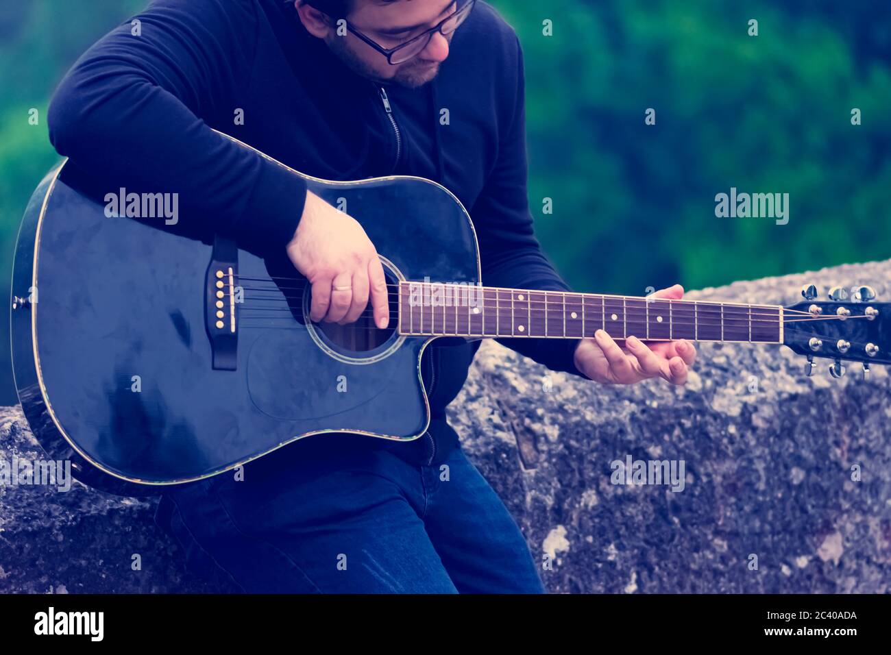 Junger Mann, der Gitarre spielt und sich gegen die Brücke lehnt Stockfoto