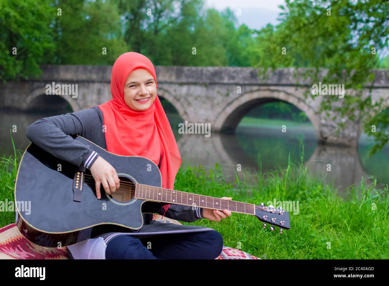 Ziemlich junge muslimische Mädchen versuchen, akustische Gitarre am Flussufer zu spielen Stockfoto