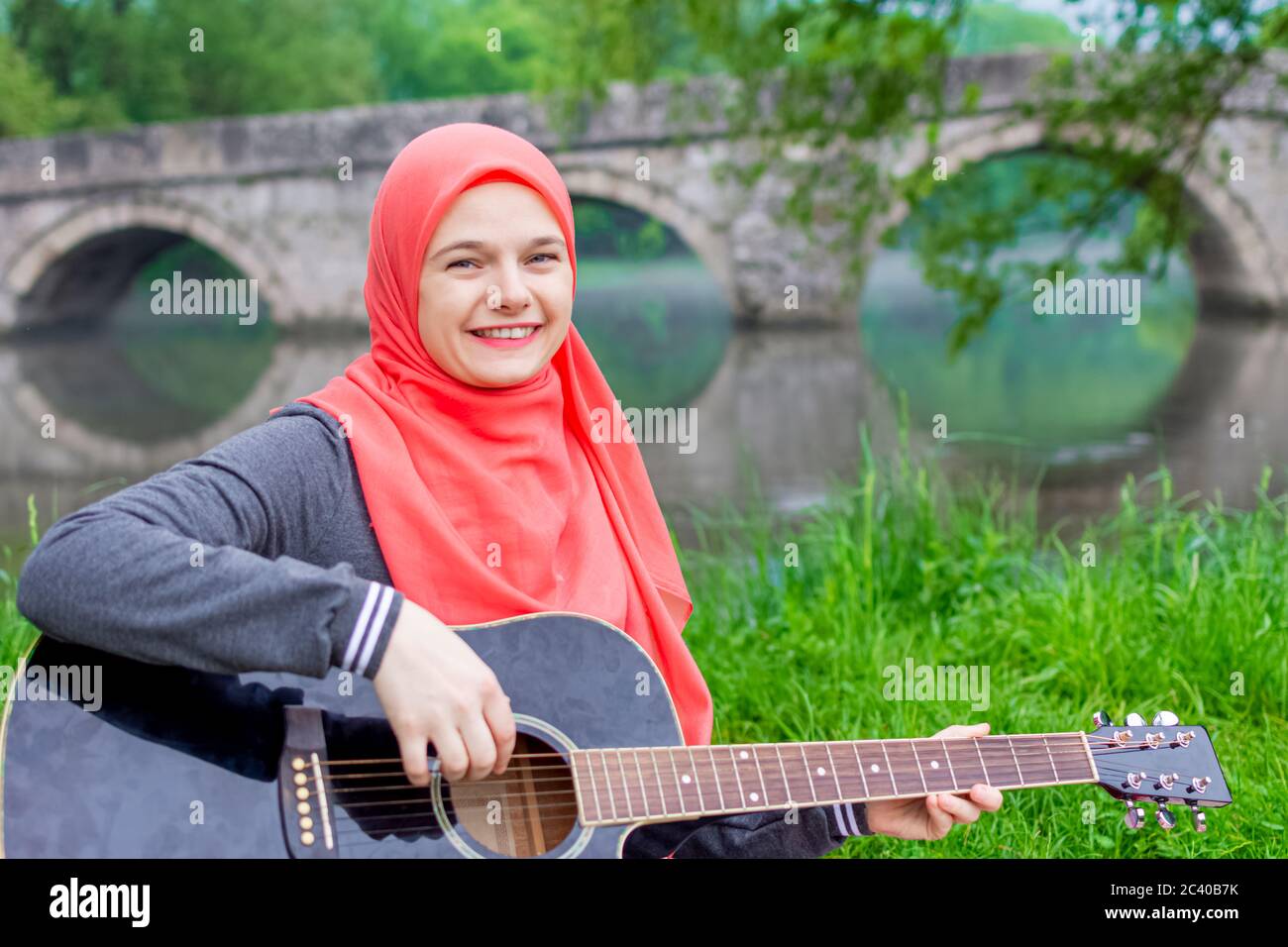 Happy Muslim Mädchen versuchen, akustische Gitarre auf dem Flussufer zu spielen Stockfoto