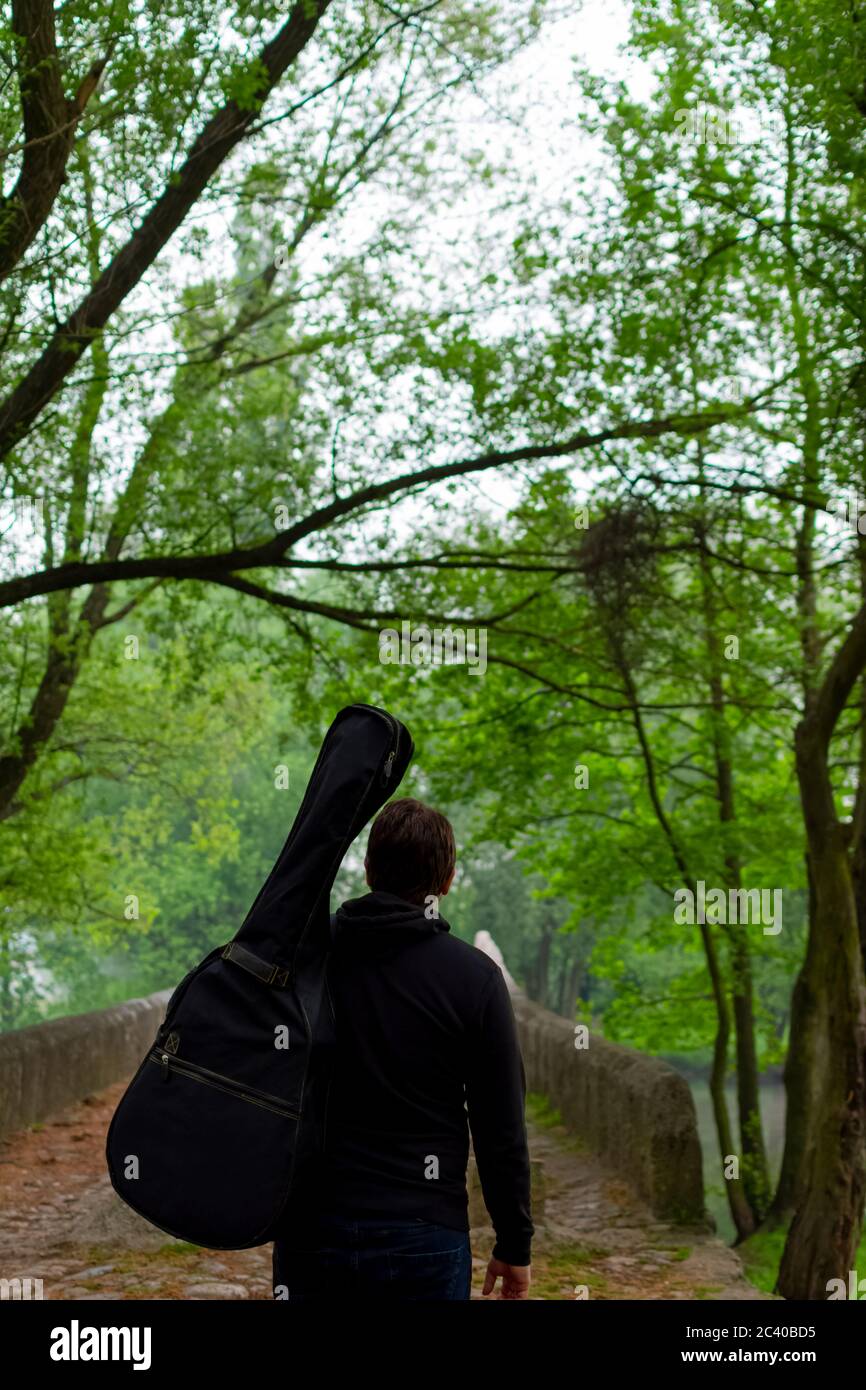 Junger Mann trägt eine Gitarrentasche, während er durch den Wald geht Stockfoto