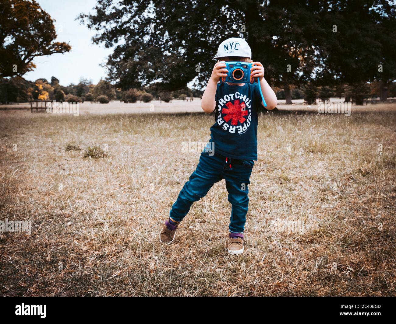 Ein kleines Kind im Freien und trägt eine Baseballmütze und T-Shirt ein Fotografieren mit einer Kamera für Kinder entwickelt Stockfoto