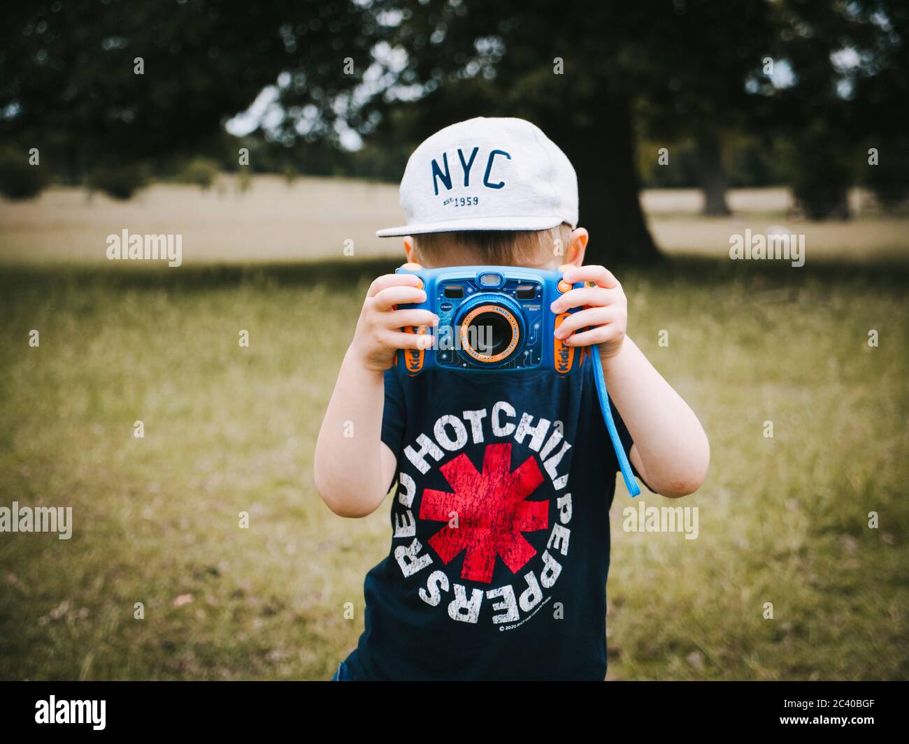 Ein kleines Kind im Freien und trägt eine Baseballmütze und T-Shirt ein Fotografieren mit einer Kamera für Kinder entwickelt Stockfoto