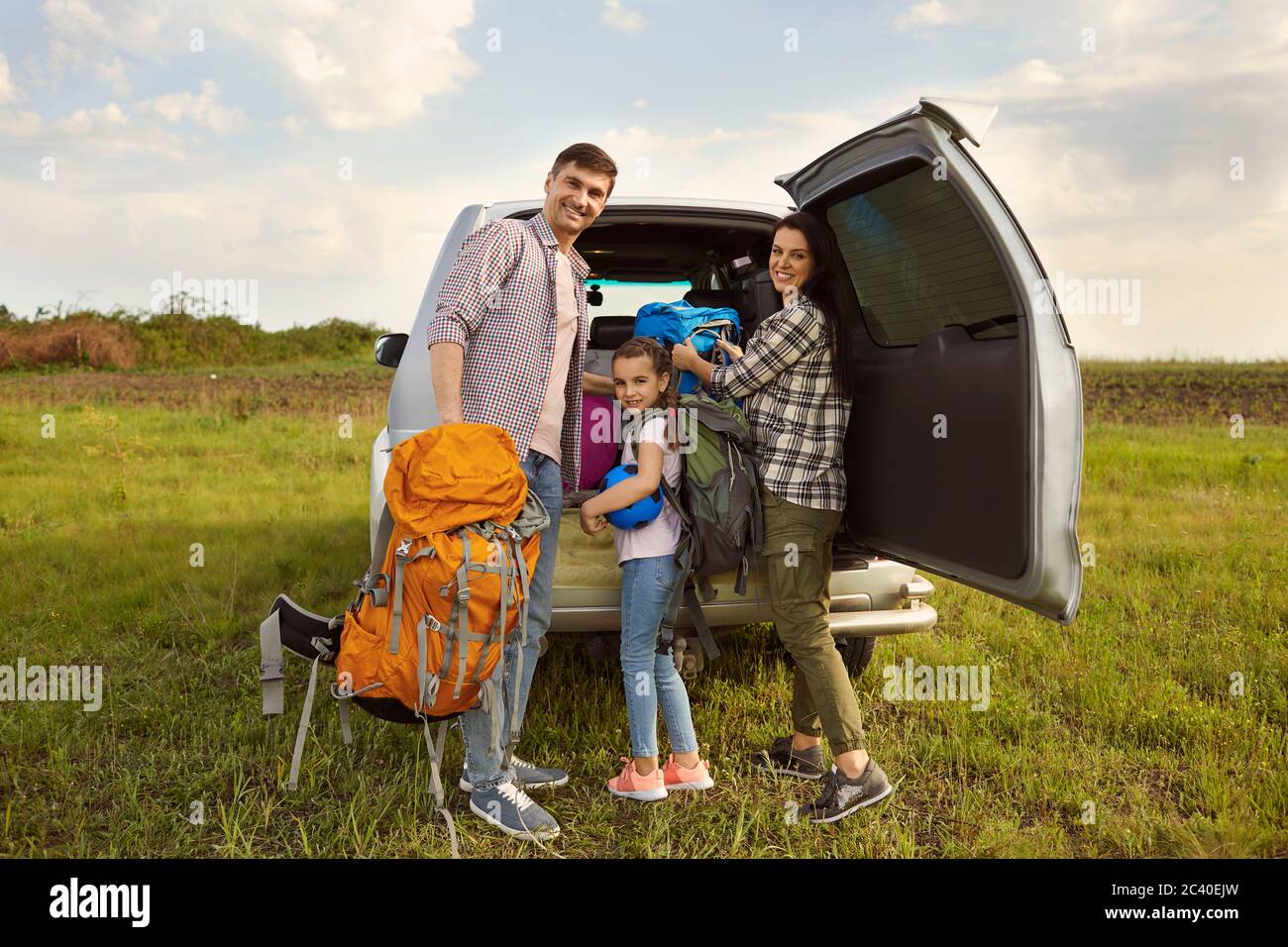 Glückliche Eltern und Töchterreisende nehmen Rucksäcke aus einem Auto zum Wandern in der Natur. Stockfoto