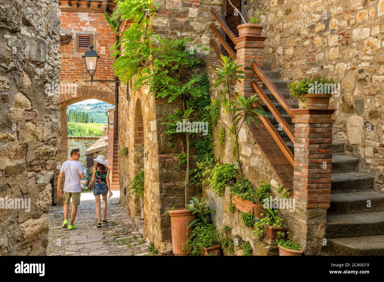 Ein paar Touristen gehen eine Gasse des Dorfes Montefioralle, in der Nähe von Greve in Chianti, im warmen Licht während eines Sommerurlaubs in der Toskana Stockfoto