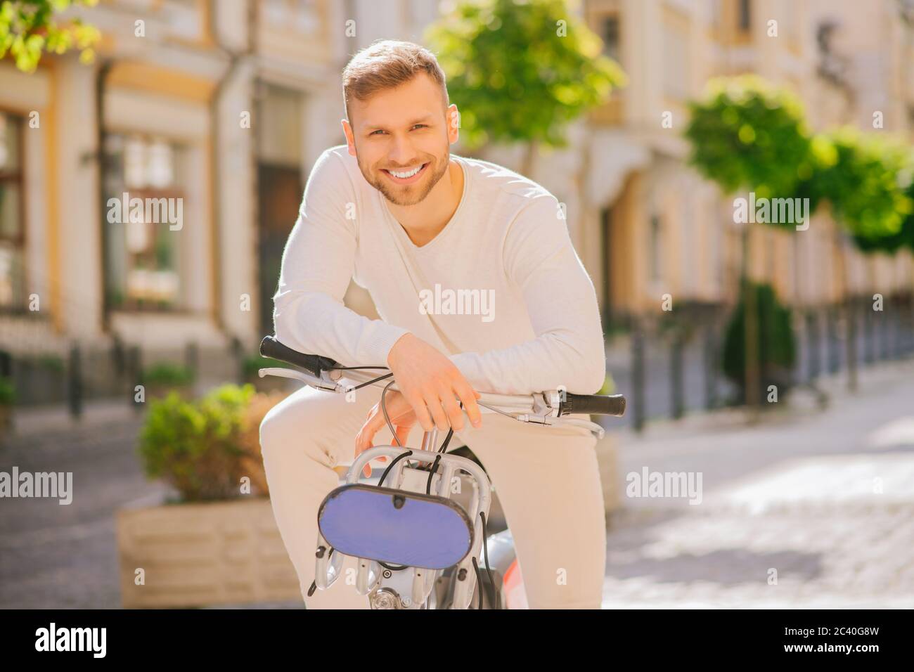 Junger erfolgreicher Kerl mit Fahrrad gelehnt Hände auf dem Lenker Stockfoto