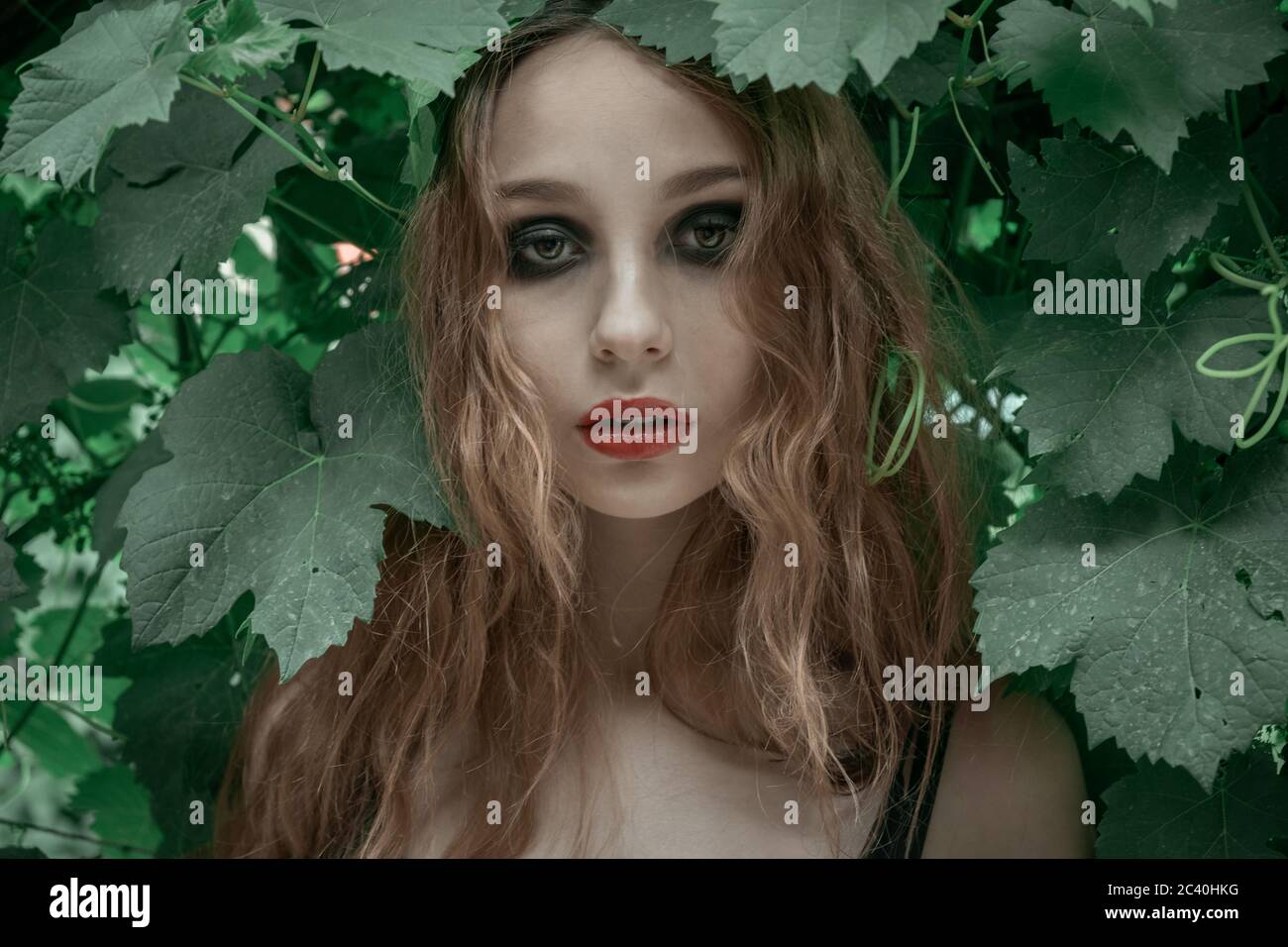 Portrait einer schönen jungen Frau mit roten Lippen vor grünen Blättern Stockfoto